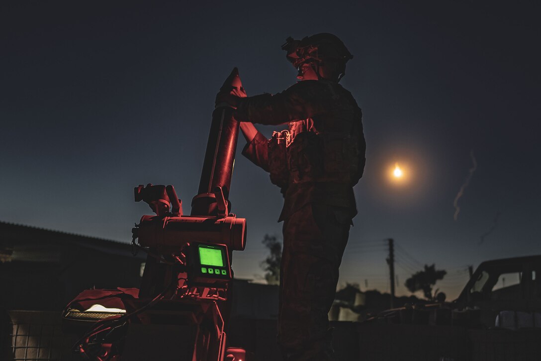 A service member is shown loading a mortar round at night.