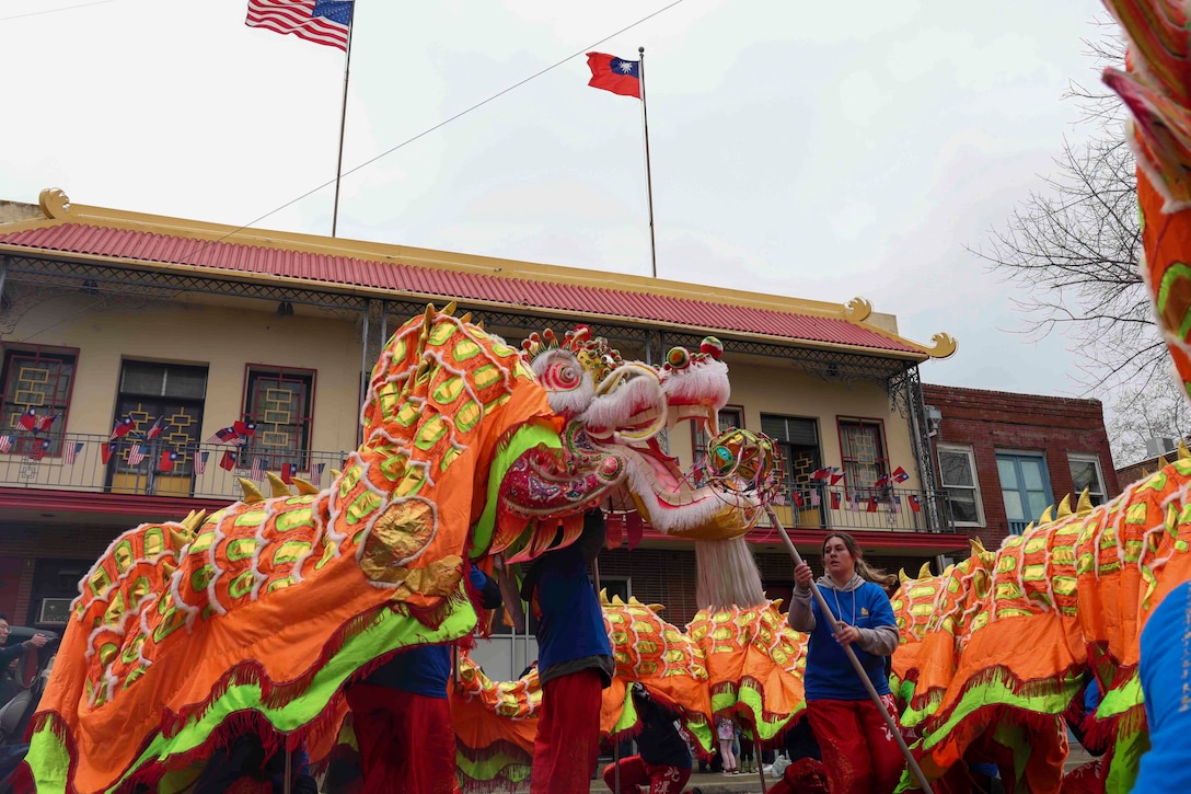 Airmen lift a costume Chinese dragon in front of a community center during a parade.