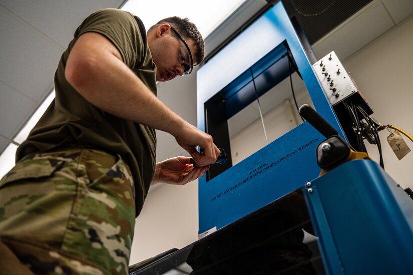 U.S. Air Force Airman 1st Class McAnally Dillan, 305th Maintenance Squadron Precision Measurement Equipment Laboratory technician, provides tension calibration readings with a deadweight tension machine at Joint Base McGuire-Dix-Lakehurst, N.J., Feb. 23, 2023. PMEL technicians at JB MDL sustain the Joint Force by providing precise, reliable and traceable equipment to mission partners across the tri-state area. (U.S. Air Force photo by Senior Airman Sergio Avalos)