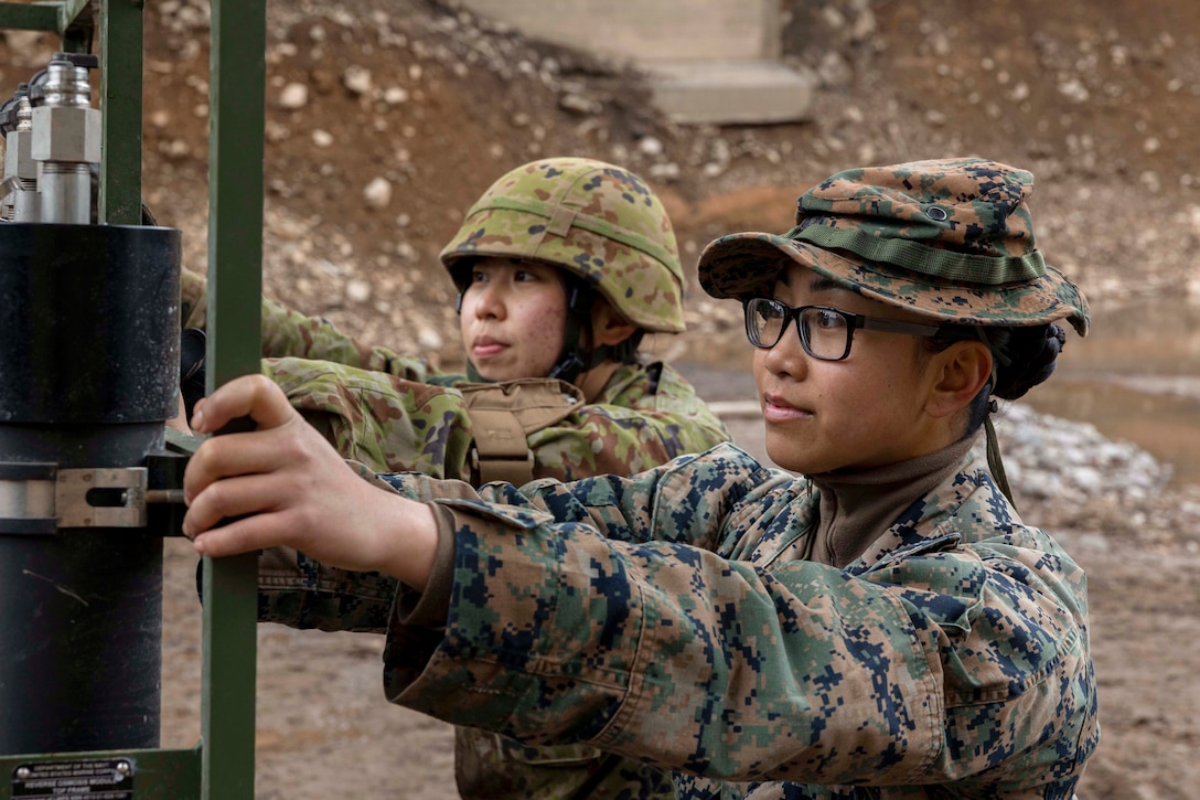 A U.S. Marine and a Japanese soldier push a purification system on a muddy road.