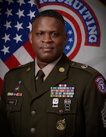 man in u.s. army uniform standing in front two flags.