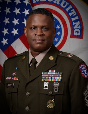 man in u.s. army uniform standing in front two flags.