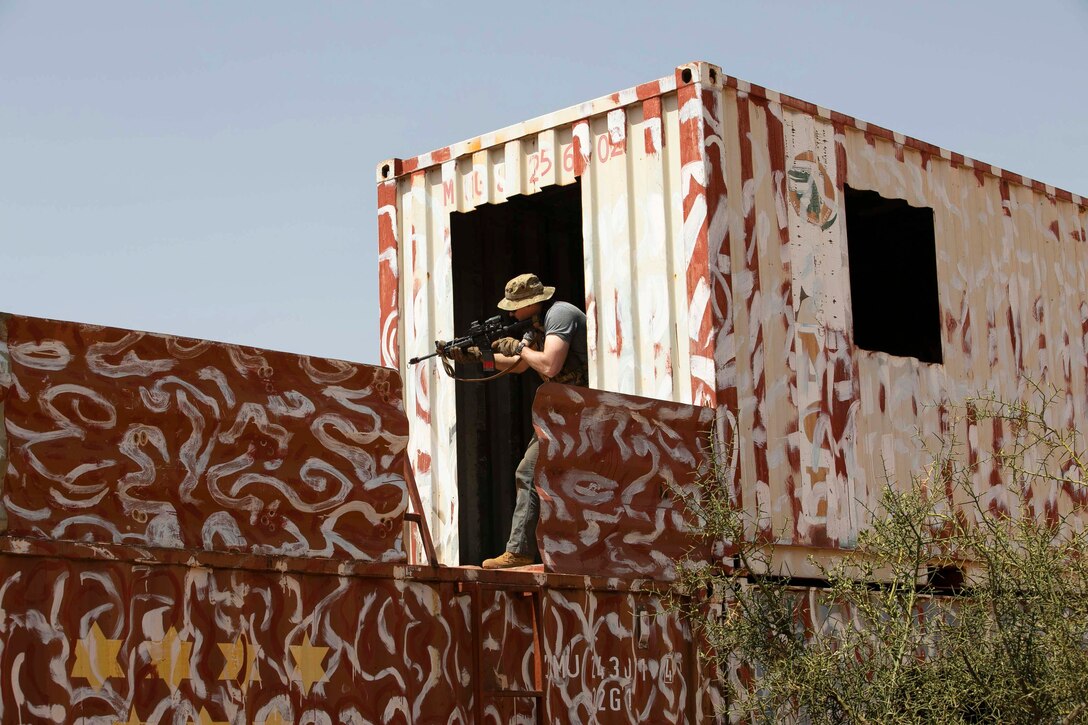 A soldier points a weapon from inside the doorframe of a building.