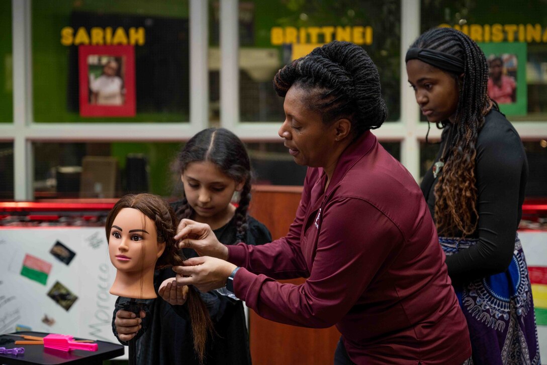 Carla Jones, Joint Base Langley-Eustis Youth Program assistant, demonstrates placing rice into hair braided by members of the JBLE Youth Program at a Black History Month event at JBLE, Virginia, Feb. 22, 2023.