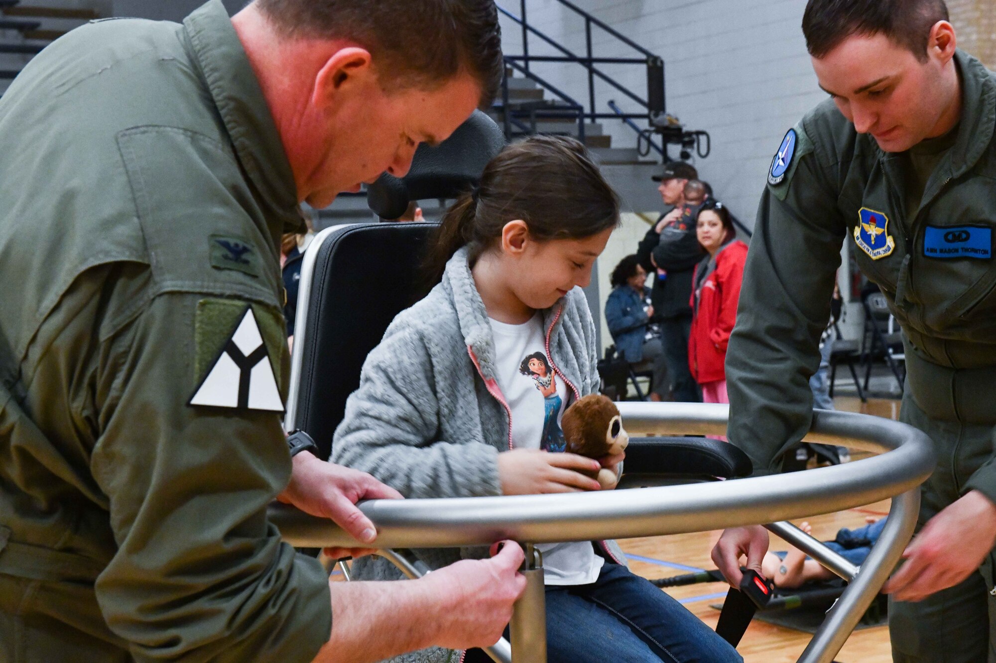 U.S. Air Force Col. Daniel Roberts, 97th Medical Group commander, and Airman Mason Thornton, 80th Operations Support Squadron aerospace physiologist, strap a child into a Barany chair during an aviation fair at Altus Junior High School, Altus, Oklahoma, Feb. 25, 2023. The Barany chair is used to invoke spatial disorientation, similar to what pilots may experience in flight. (U.S. Air Force photo by Airman 1st Class Miyah Gray)