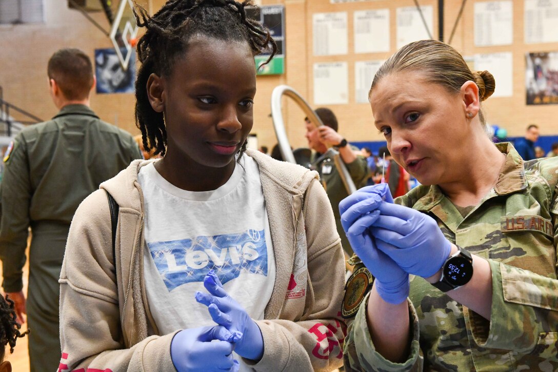 U.S. Air Force Tech. Sgt. Leslie Hines, 97th Operational Medical Readiness Squadron flight medicine flight chief, demonstrates to a community member how to use a needle at the aviation fair at Altus Junior High School, Altus, Oklahoma, Feb. 25, 2023. Flight medicine personnel demonstrated how to give CPR, set up IV lines and spun guests in a barbary chair to simulate spatial disorientation. (U.S. Air Force photo by Airman 1st Class Miyah Gray)