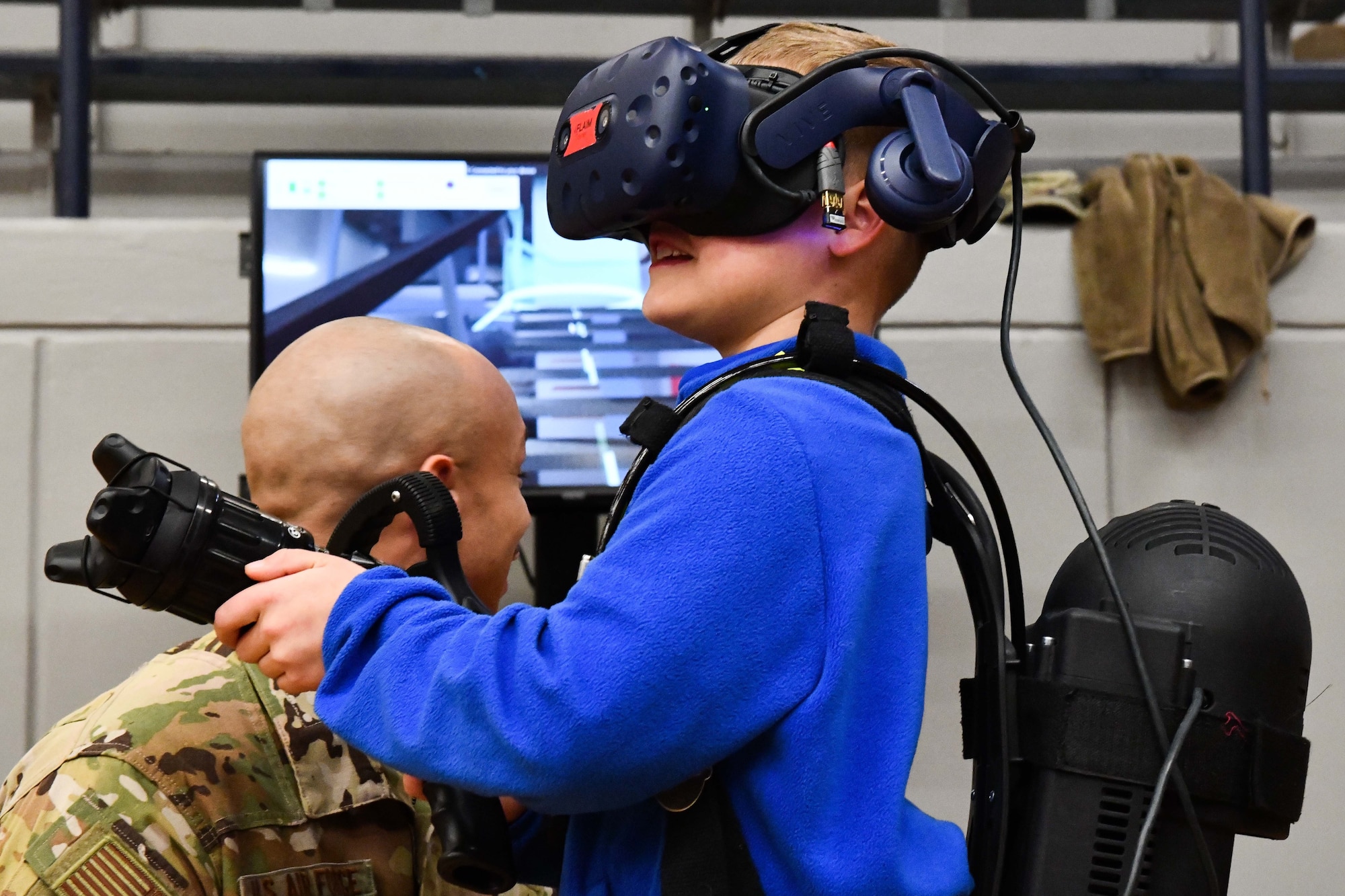 U.S. Air Force Staff Sgt. Payton Terry, 97th Civil Engineer Squadron firefighter crew chief, assists a child in operating a FLAIM trainer during an aviation fair at Altus Junior High School, Altus, Oklahoma, Feb. 25, 2023. The FLAIM trainer is used by firefighters as a virtual tool for maneuvering different emergency scenarios that may occur on the job. (U.S. Air Force photo by Airman 1st Class Miyah Gray)