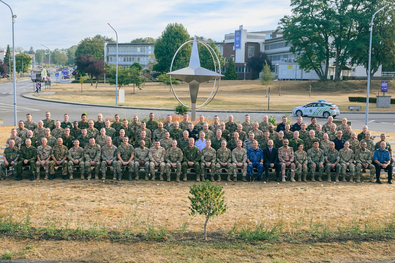 A large group of foreign and domestic uniformed service members sit on bleachers for a photo.