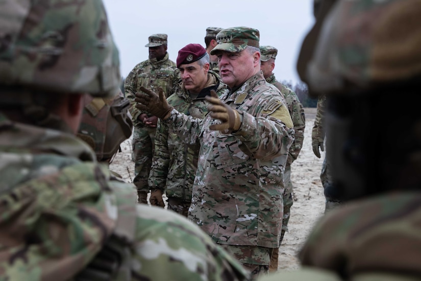 An older man dressed in a military uniform gestures as other service members look on.