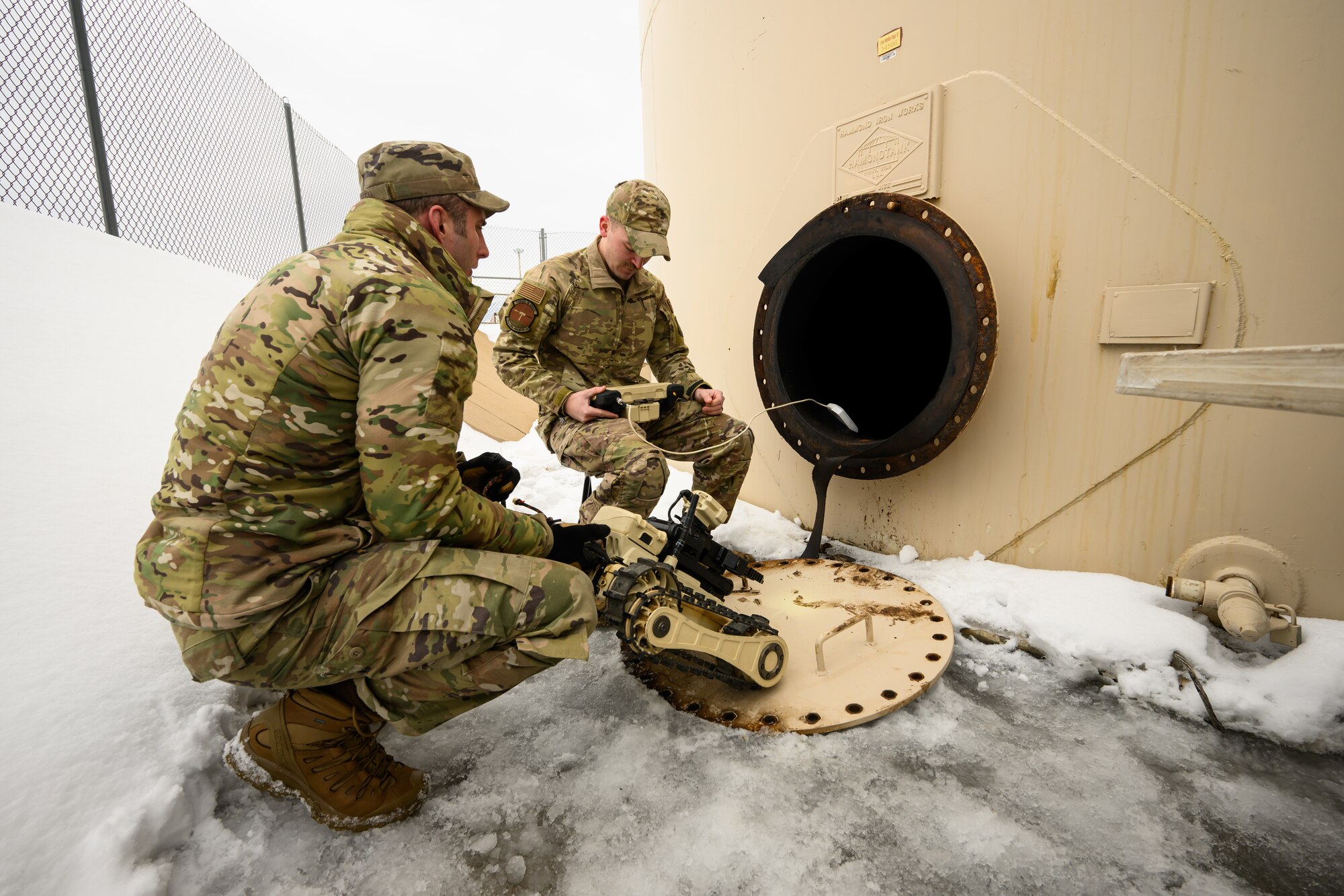 Two airmen prepare to drive a robot into a fuel tank