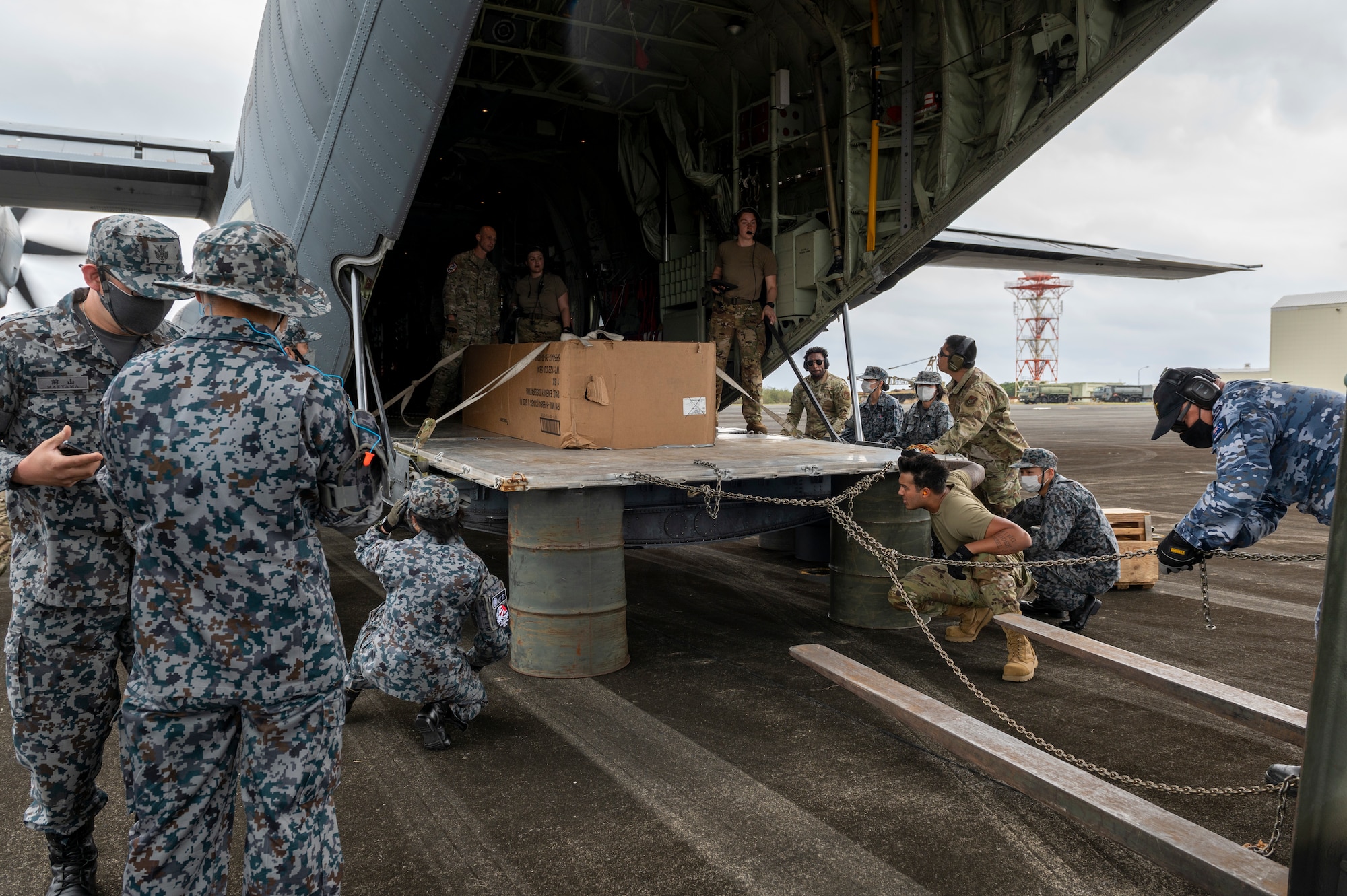 A team of U.S. Air Force, Japan Maritime Self-Defense Force, and Royal Australian Air Force members pull a large cargo pallet from a 36th Airlift Squadron C-130J Super Hercules onto storage barrels using combat offloading during the Cope North 23 exercise, on the remote island of Iwo Jima, Japan, Feb. 21, 2023.
