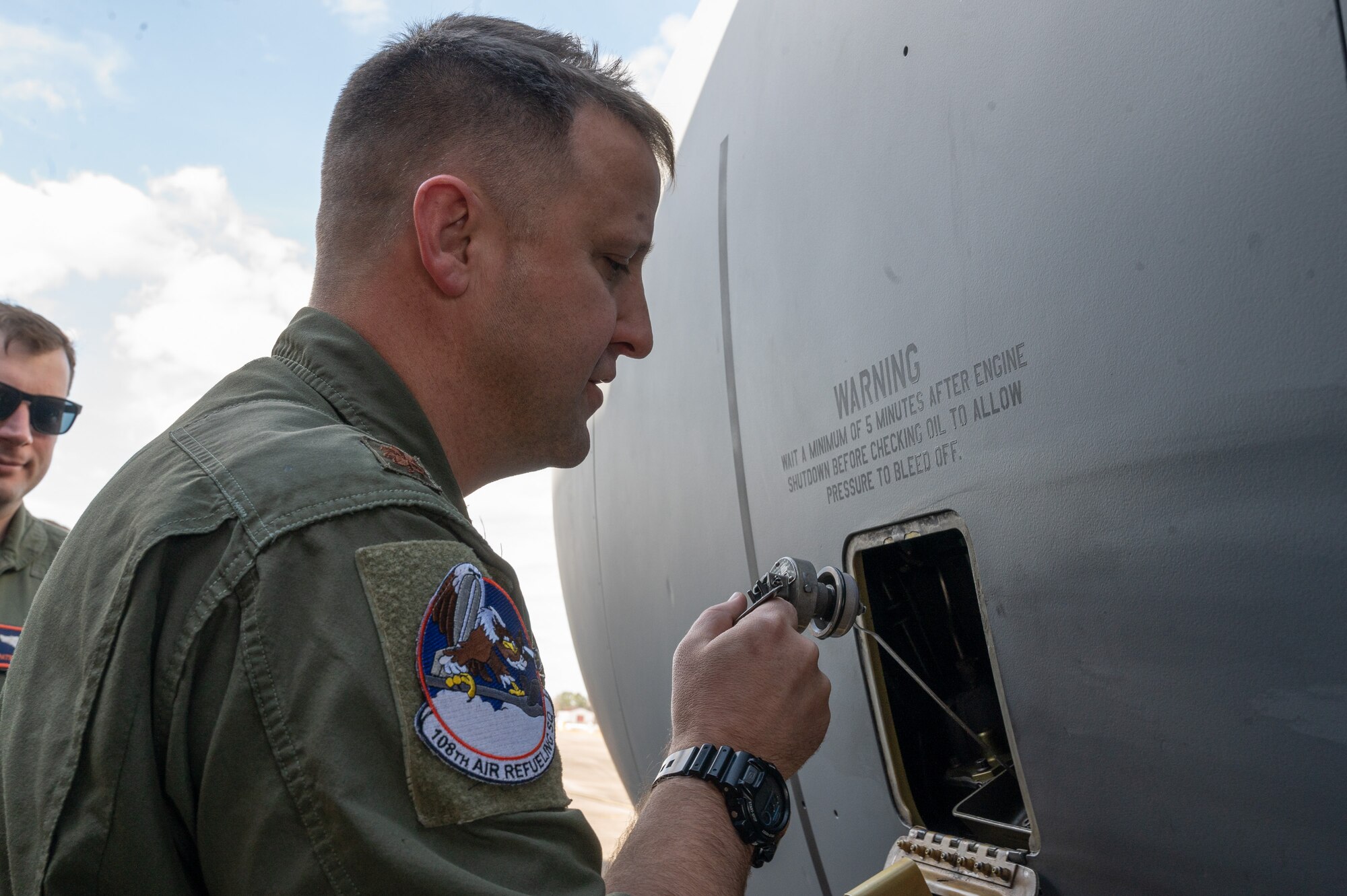 A U.S. Air Force pilot checks the oil level on a KC-135 engine through a small access panel on the side of the engine.