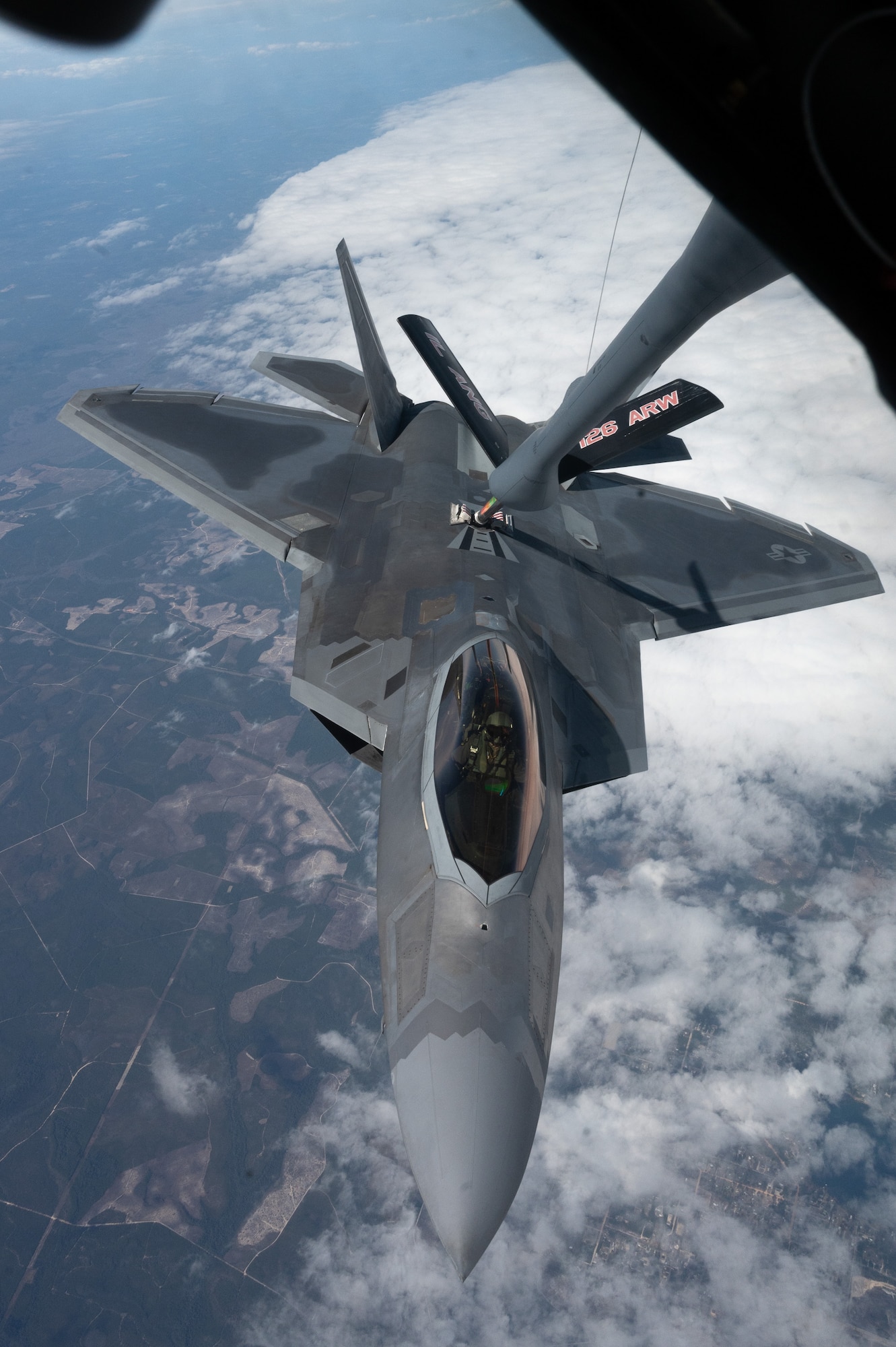 A U.S. Air Force F-22 Raptor flies close to a KC-135 while a refueling boom is attached to its fuel port.