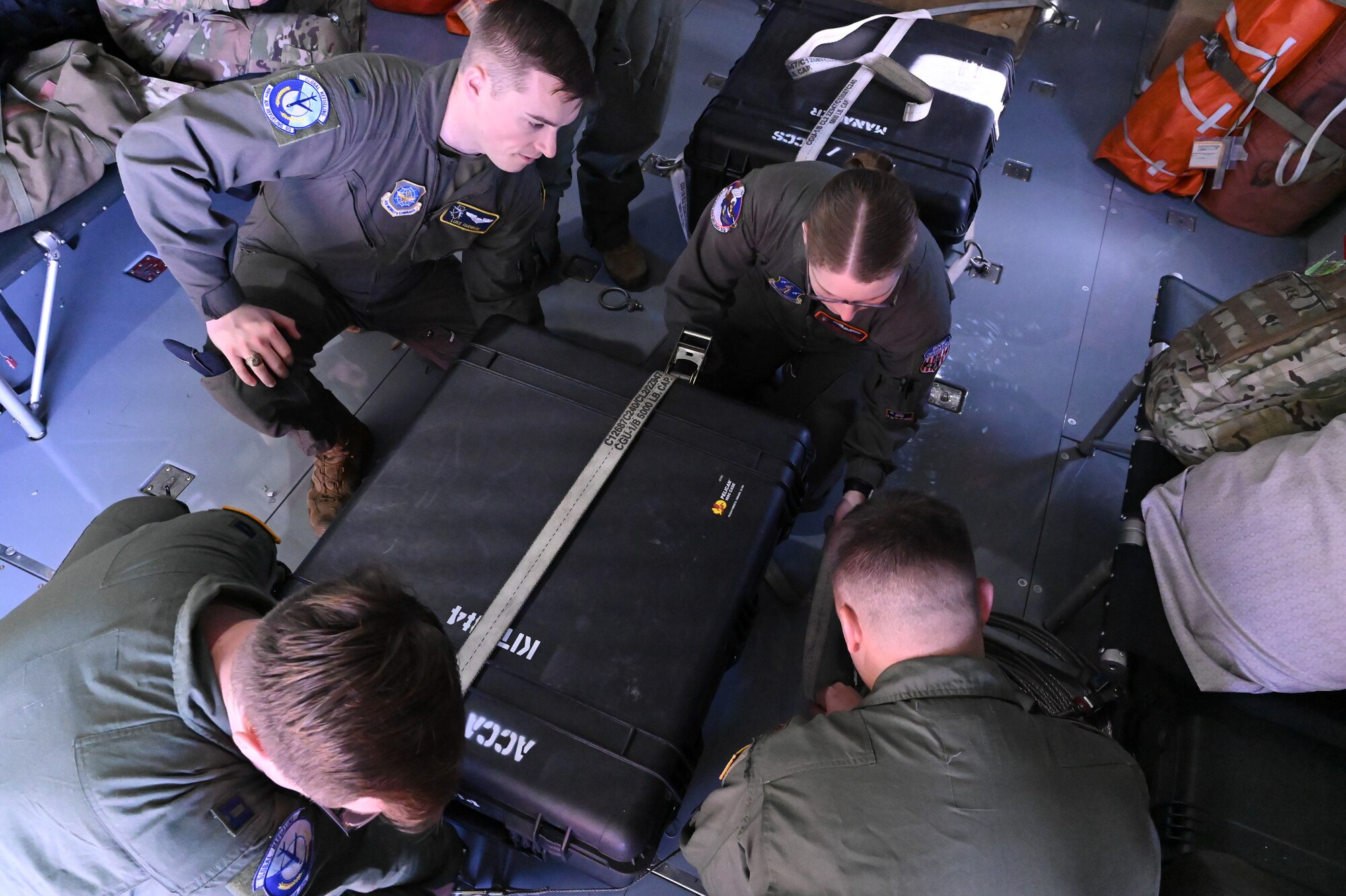Four U.S. Air Force members are kneeling down to secure a small crate with cargo straps on the floor of a KC-135.