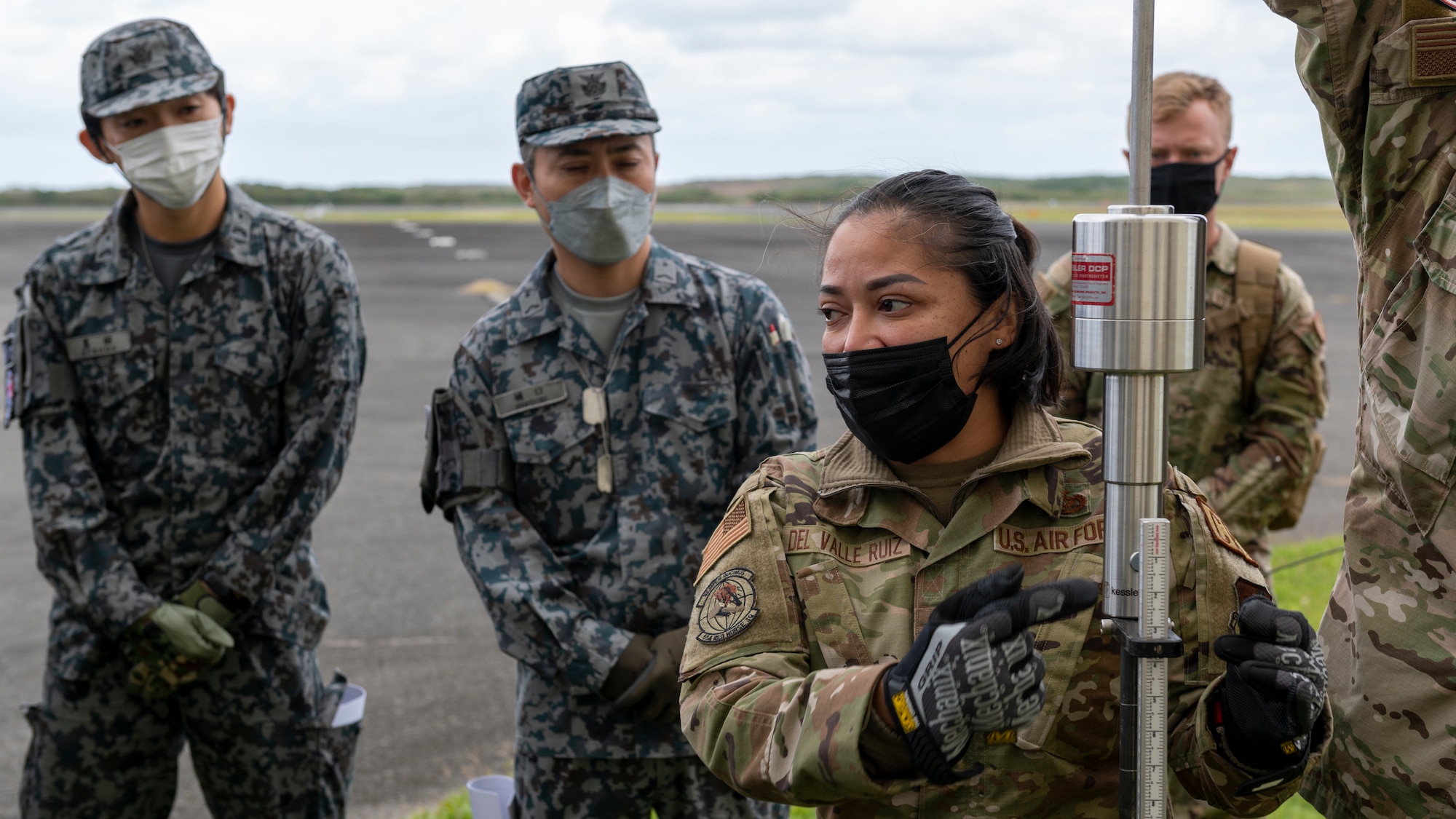 U.S. Air Force Master Sgt. Yelida Del Valle Ruiz, 554th Red Horse Squadron contingency airfield pavement evaluator, instructs Japan Maritime Self-Defense Force members on how to use a Dynamic Cone Penetrometer (DCP) for airfield survey operations during the Cope North 23 exercise, on the remote island of Iwo Jima, Japan, Feb. 21, 2023.