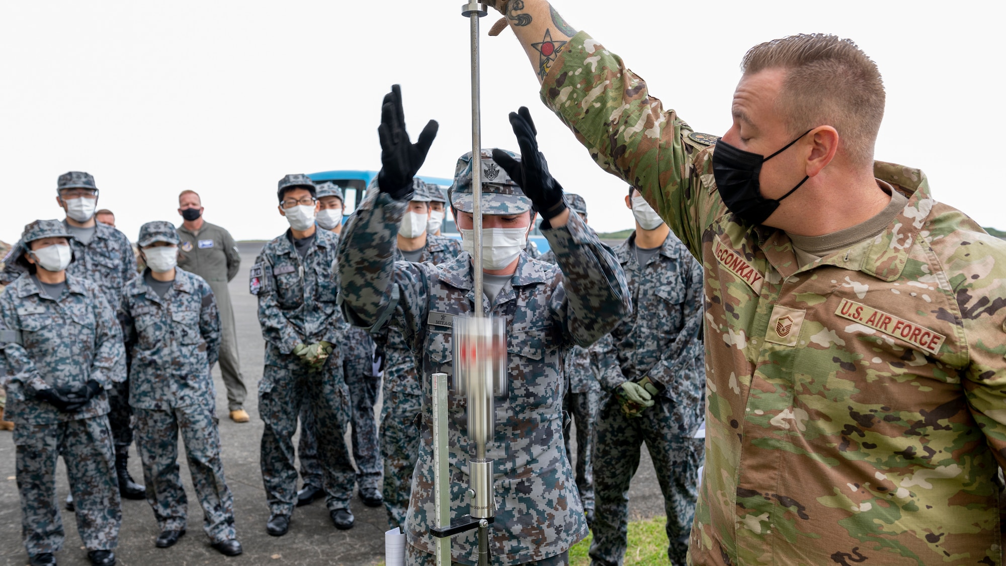 U.S. Air Force Master Sgt. Andrew McConkay, 36th Operations Support Squadron airfield manager, holds a Dynamic Cone Penetrometer (DCP) steady for Japan Maritime Self-Defense Force Senior Airman Aya Mukai, security specialist, as he drops a calibrated weight onto a measuring spike while conducting airfield survey operations during the Cope North 23 exercise, on the remote island of Iwo Jima, Japan, Feb. 21, 2023.