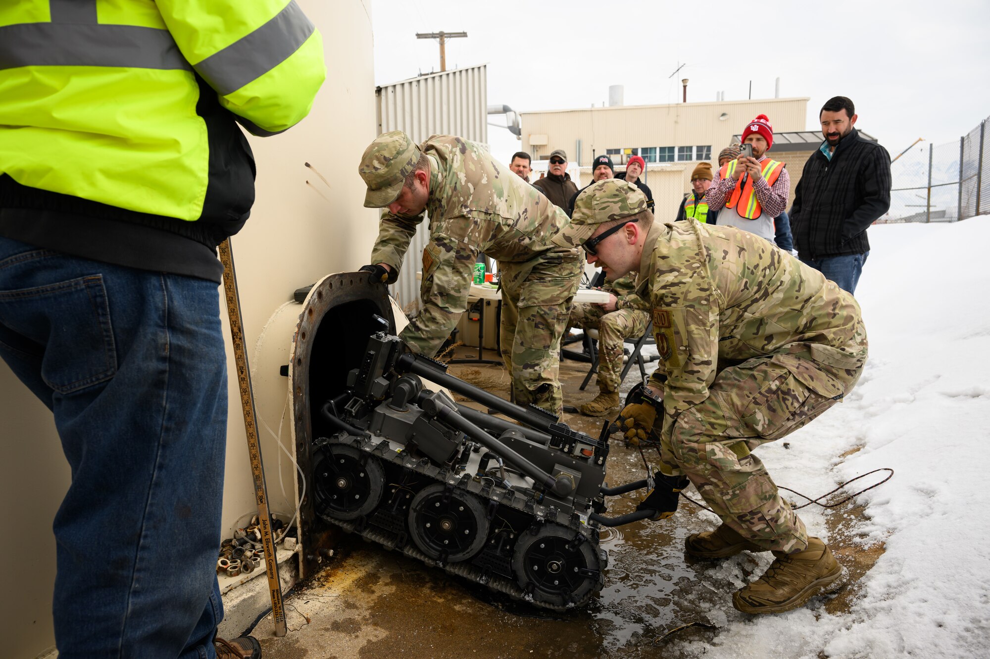 two airmen guide a robot into a fuel tank