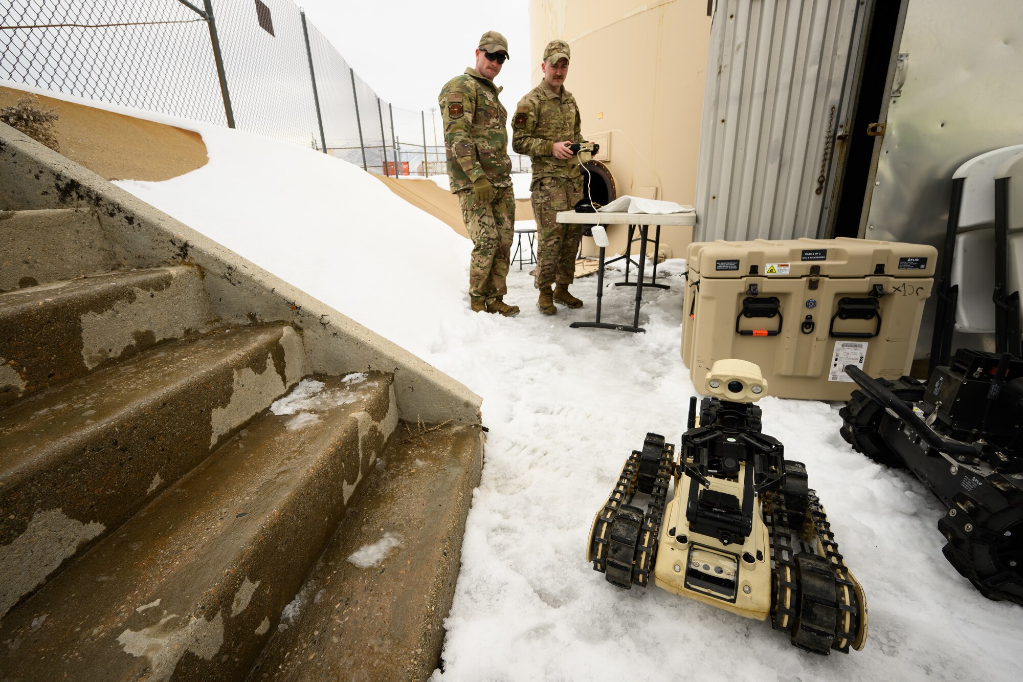 Two airmen drive a robot along the snow covered ground