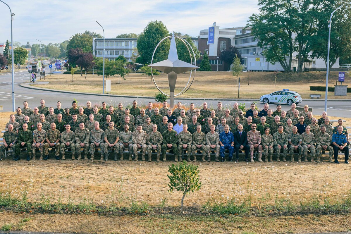 A large group of foreign and domestic uniformed service members sit on bleachers for a photo.