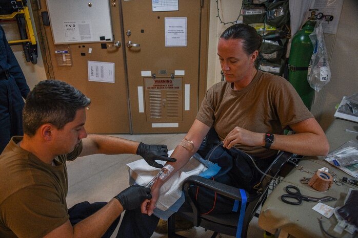 221221-N-TC338-1101 INDIAN OCEAN (Dec. 21, 2022) Lt. Scott Yusko, a Role 2 Light Maneuver (R2LM) Critical Care (CC) Nurse, left, performs a blood transfusion with Lt. Mia Galassi, an R2LM Certified Registered Nurse Anesthetist (CRNA) aboard the expeditionary sea base USS Hershel "Woody" Williams (ESB 4), Dec. 21, 2022. Hershel "Woody" Williams is on a scheduled deployment in the U.S. Naval Forces Africa area of operations, employed by U.S. Sixth Fleet to defend U.S., Allied and partner interests. (U.S. Navy photo by Mass Communication Specialist 2nd Class Conner D. Blake/Released)