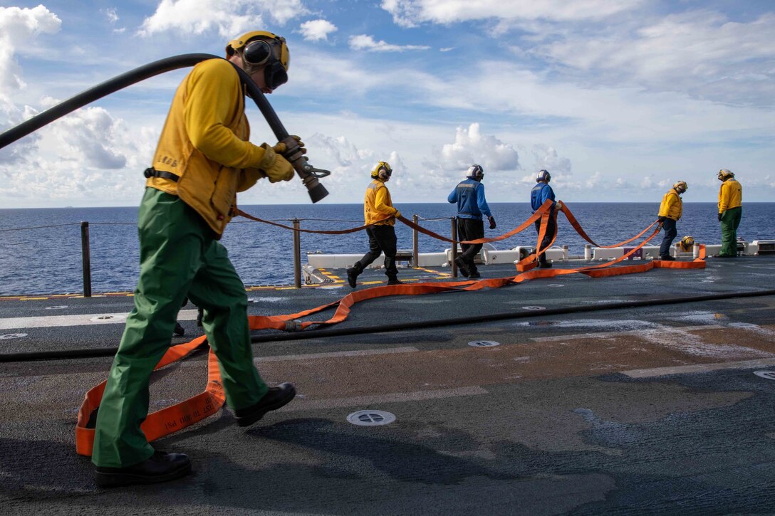 Sailors carry hoses on the deck of a ship.