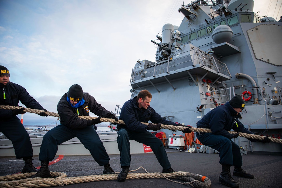 Sailors pull on a heavy rope aboard a ship.