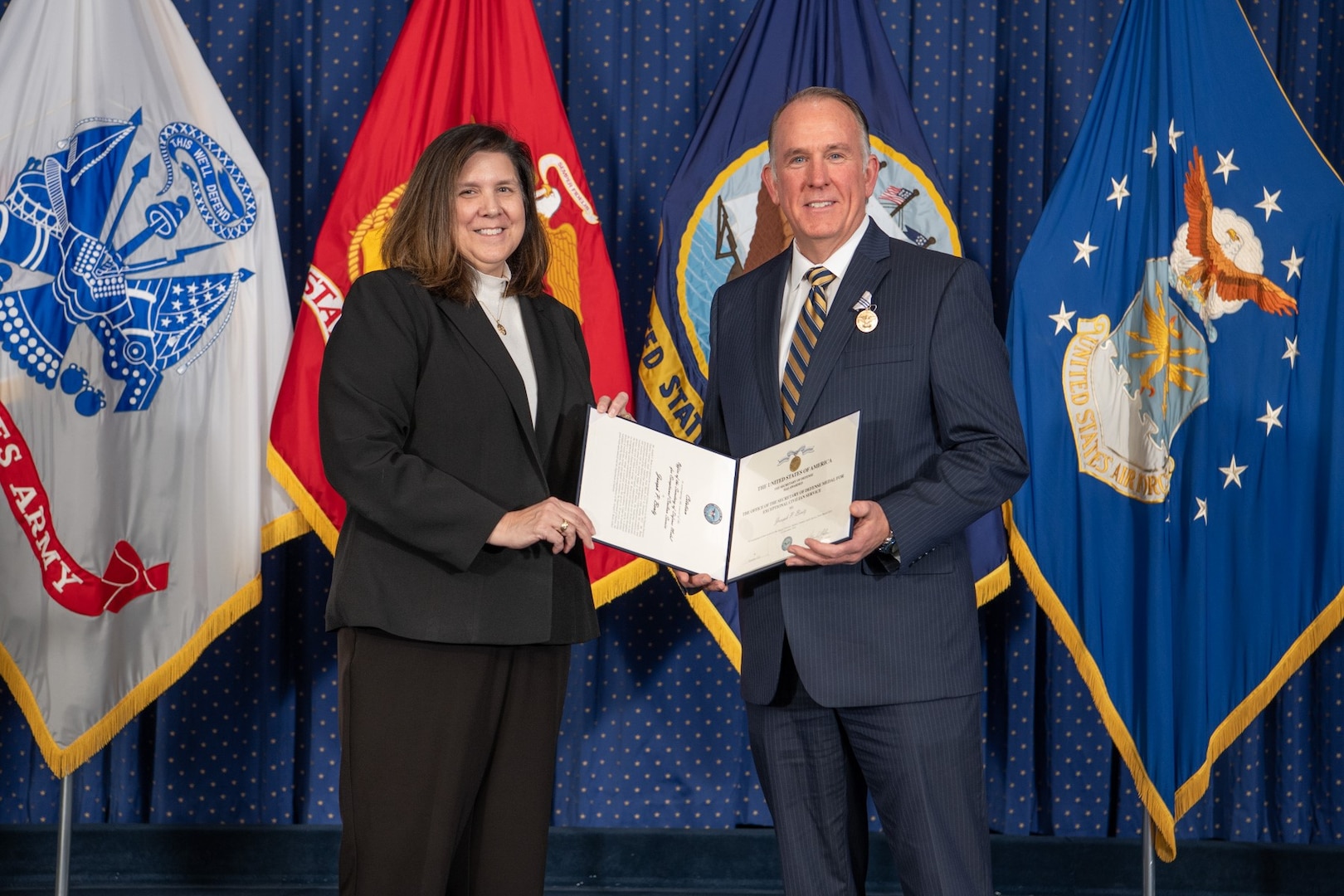 man and woman in business suits wtih service flags in background