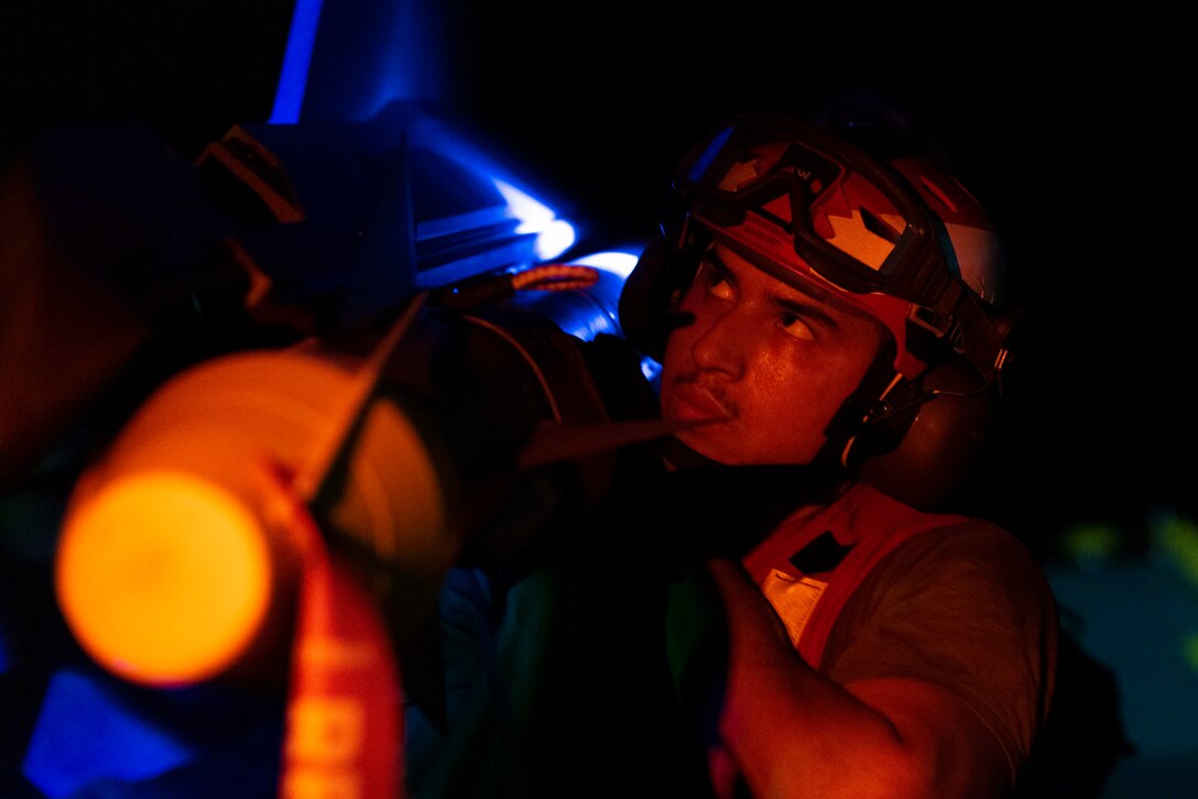 A service member in a helmet is shown close up, loading a missile to a military aircraft.