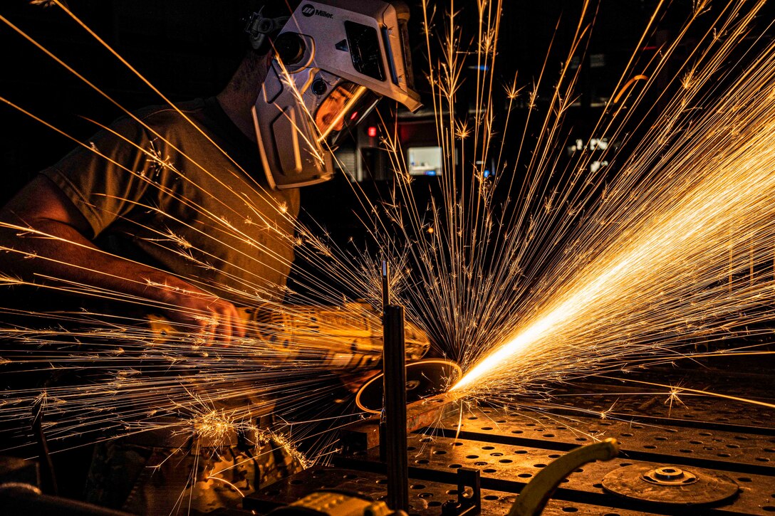 An airman uses a tool to cut a piece of metal as sparks fly.