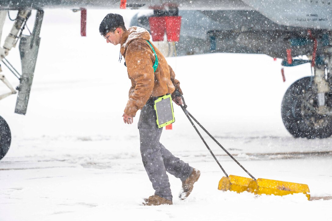 An airman pulls a chock through snow as snow falls.