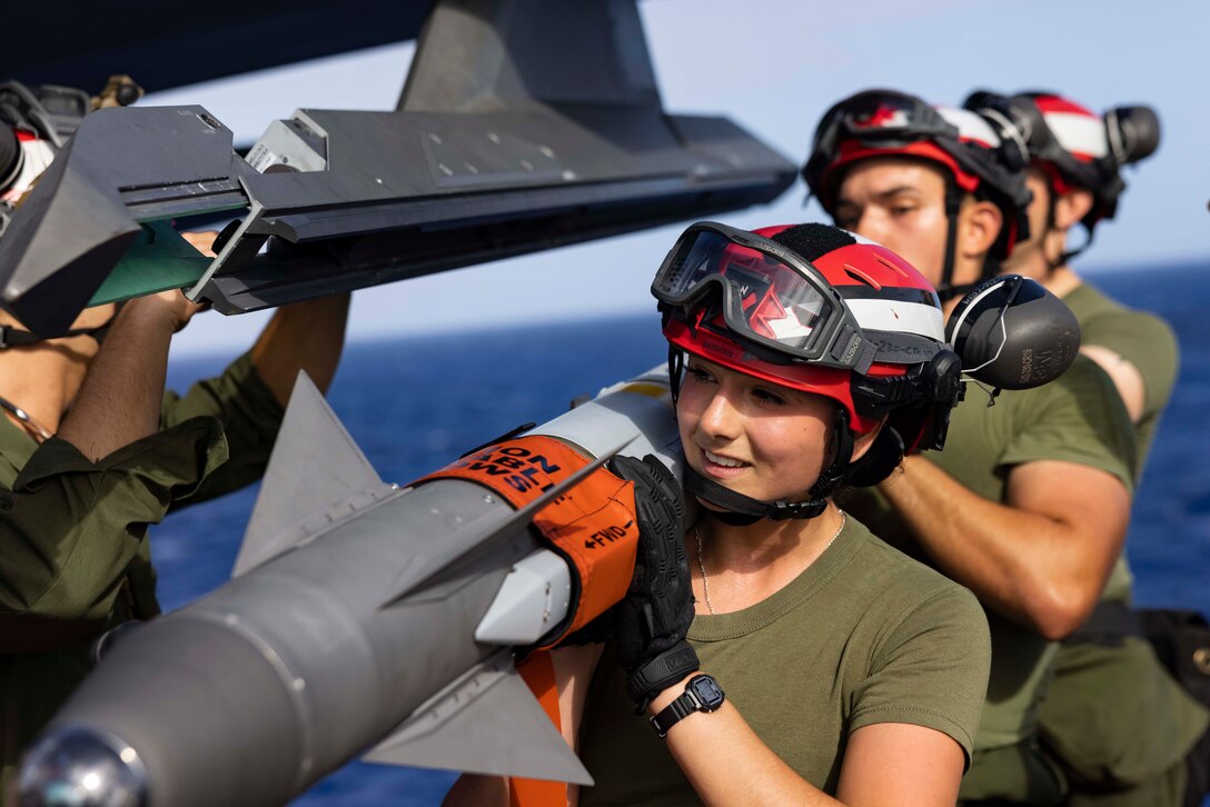 Marines carry a missile on their shoulders on a ship's deck.