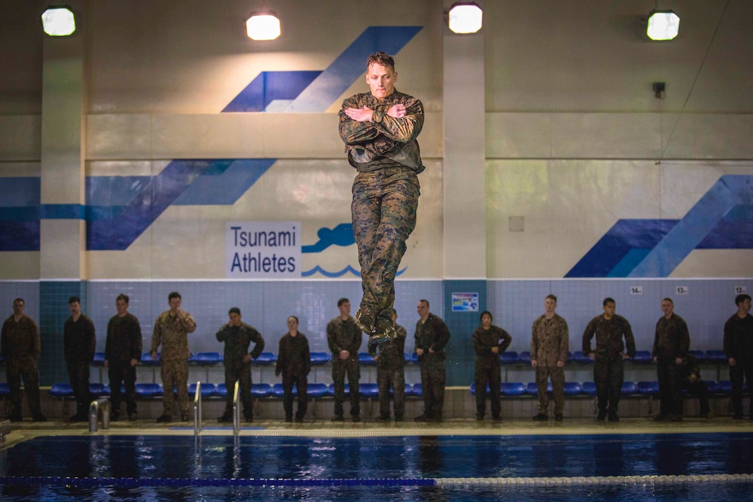 A uniformed Marine jumps into a pool during basic swim qualification.