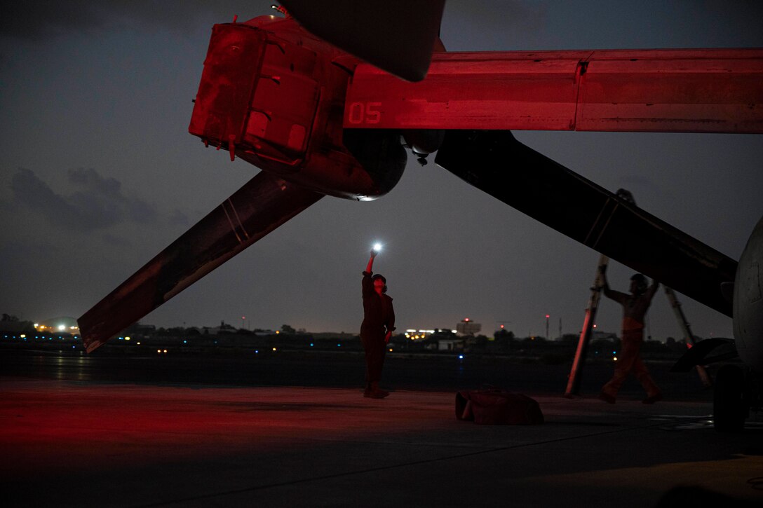 A Marine holds a flashlight up to an aircraft in the dark.