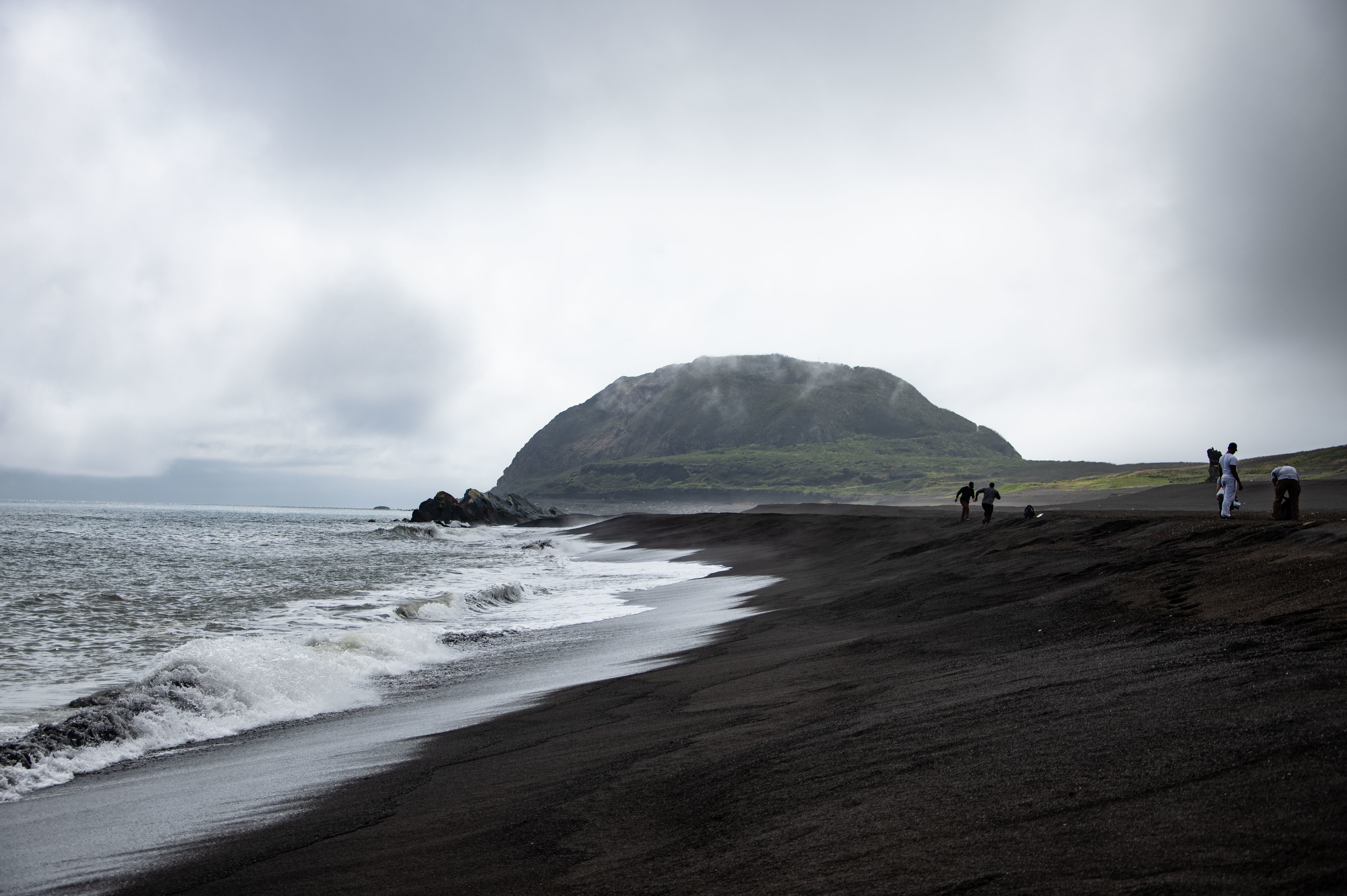 The tide on a dark beach with a distant island in the background.