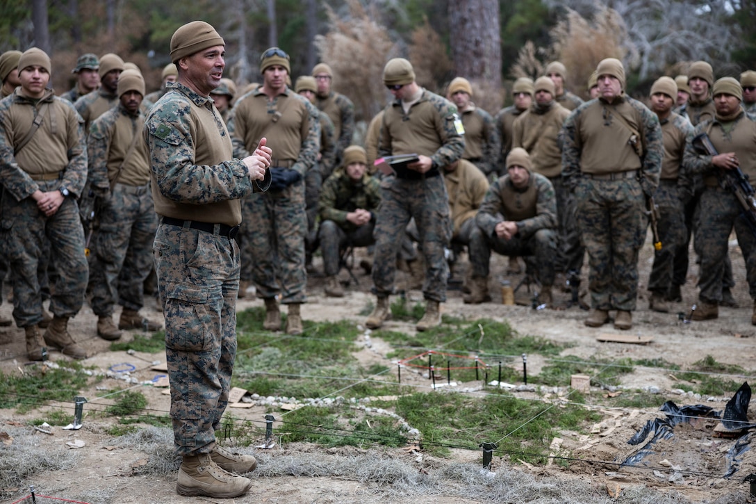 U.S. Marine Corps Lt. Col. Scott Helminski, commanding officer of Battalion Landing Team 1/6, 26th Marine Expeditionary Unit (MEU), addresses Marines and Sailors from across the 26th Marine Expeditionary Unit during a rehearsal of concept (ROC) over a terrain model prior to a simulated raid during Marine Expeditionary Unit Exercise (MEUEX) I at Marine Corps Auxiliary Landing Field Bogue, North Carolina, Dec. 20, 2022. The raid was the culminating MAGTF mission for the exercise. Through continued training and preparation, the 26th MEU will continue to be the nation’s premier expeditionary force-in readiness and remains ready and able to respond at a moment’s notice. (U.S. Marine Corps photo by Staff Sgt. Jesus Sepulveda Torres)