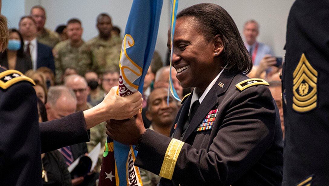 A female military service member receives a flag that is passed to her during a ceremony.