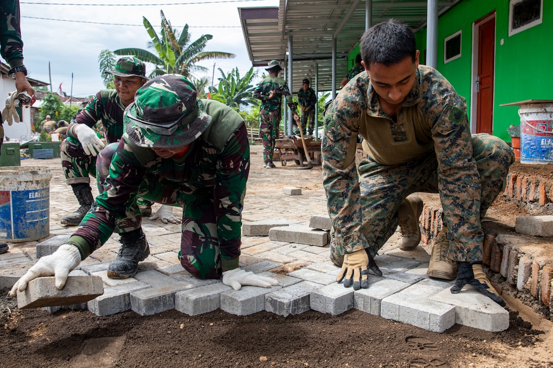 Marines kneel and build a brick path.