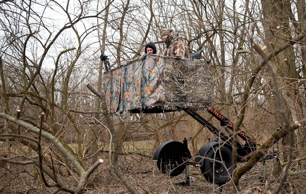 Two hunters sit in an elevated deer stand.