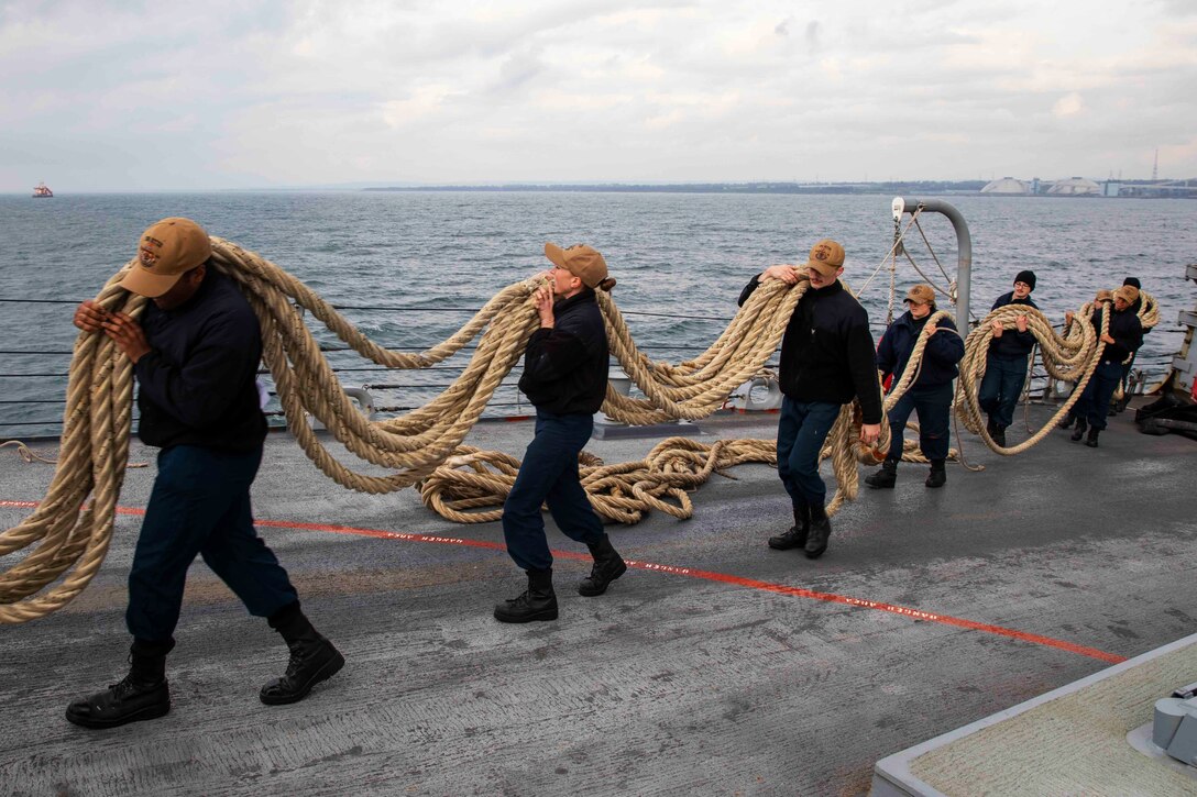 Sailors carry lines over their shoulders as the ship departs Italy following a scheduled port visit