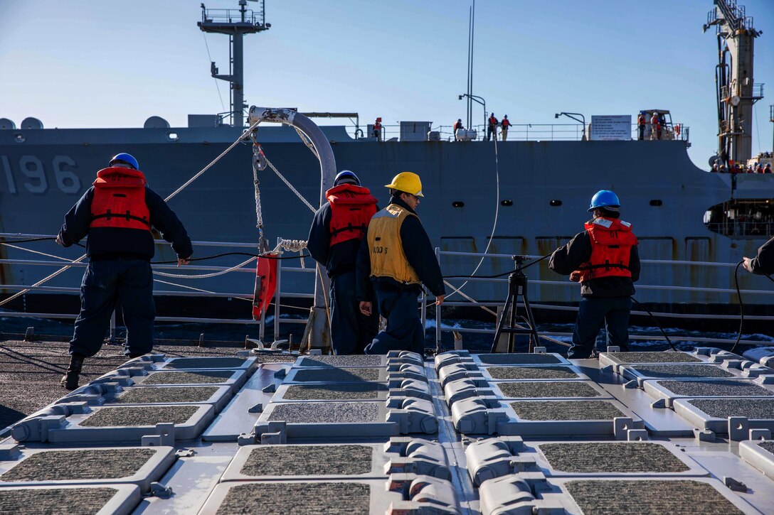 Sailors pay out a phone and distance line to a fleet replenishment oiler