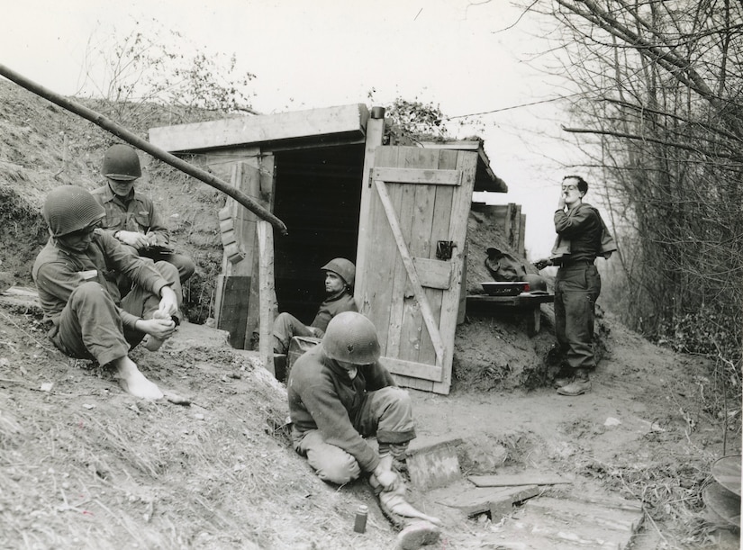 Five men relax near a bunker dug into a hill.