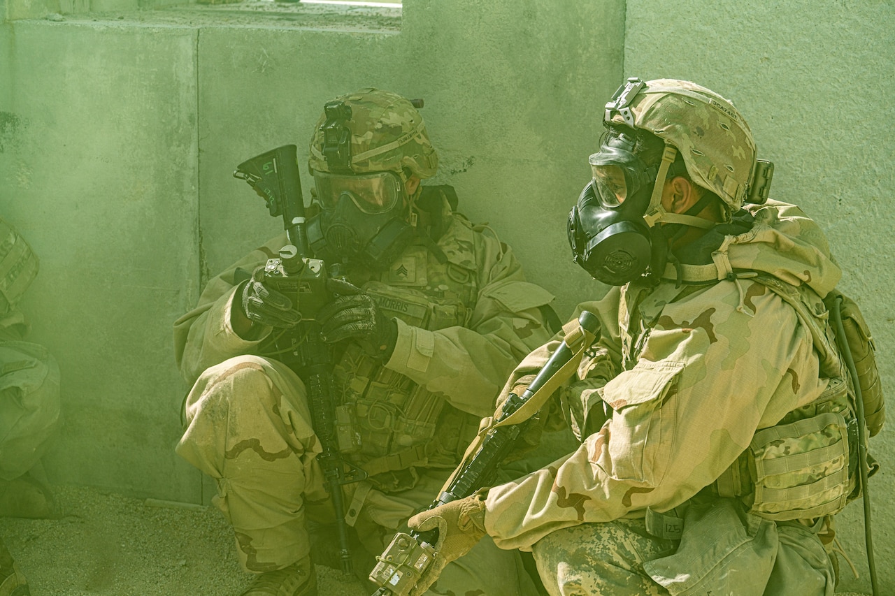 Soldiers wear gas masks as they squat on the ground in a thick haze.