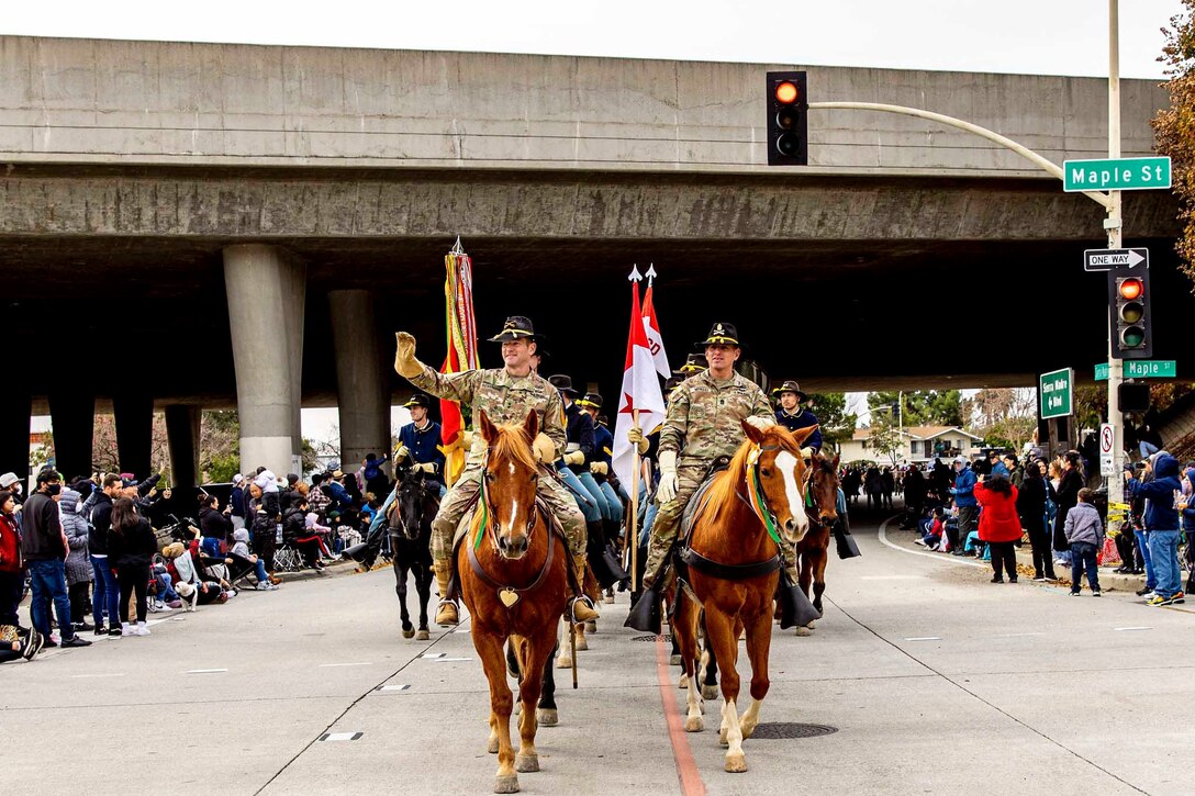 Soldiers ride on horses in front of a crowd.