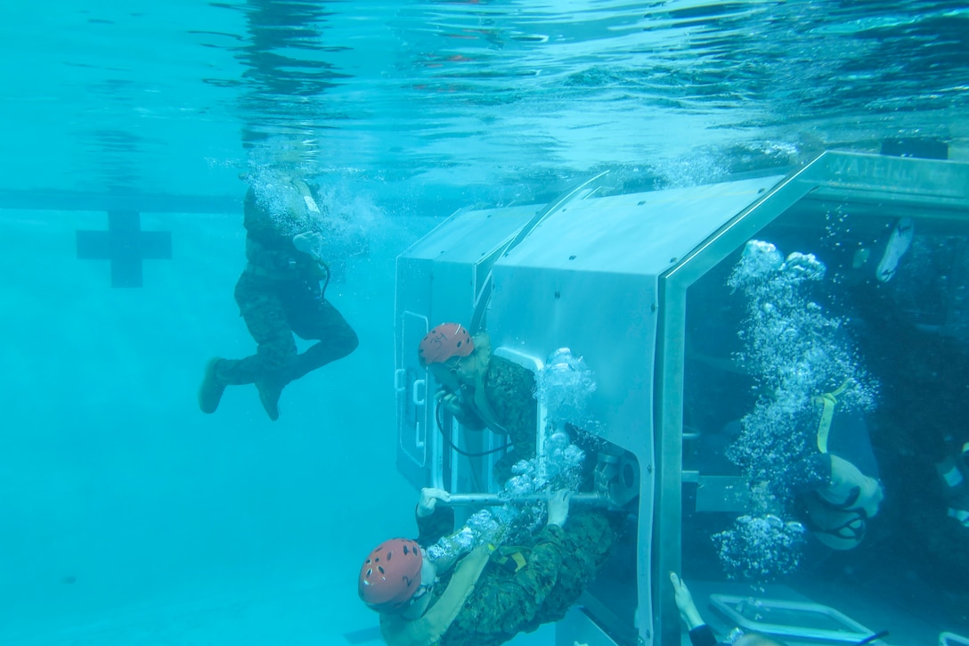 Marines exit a simulated aircraft submerged in a pool.