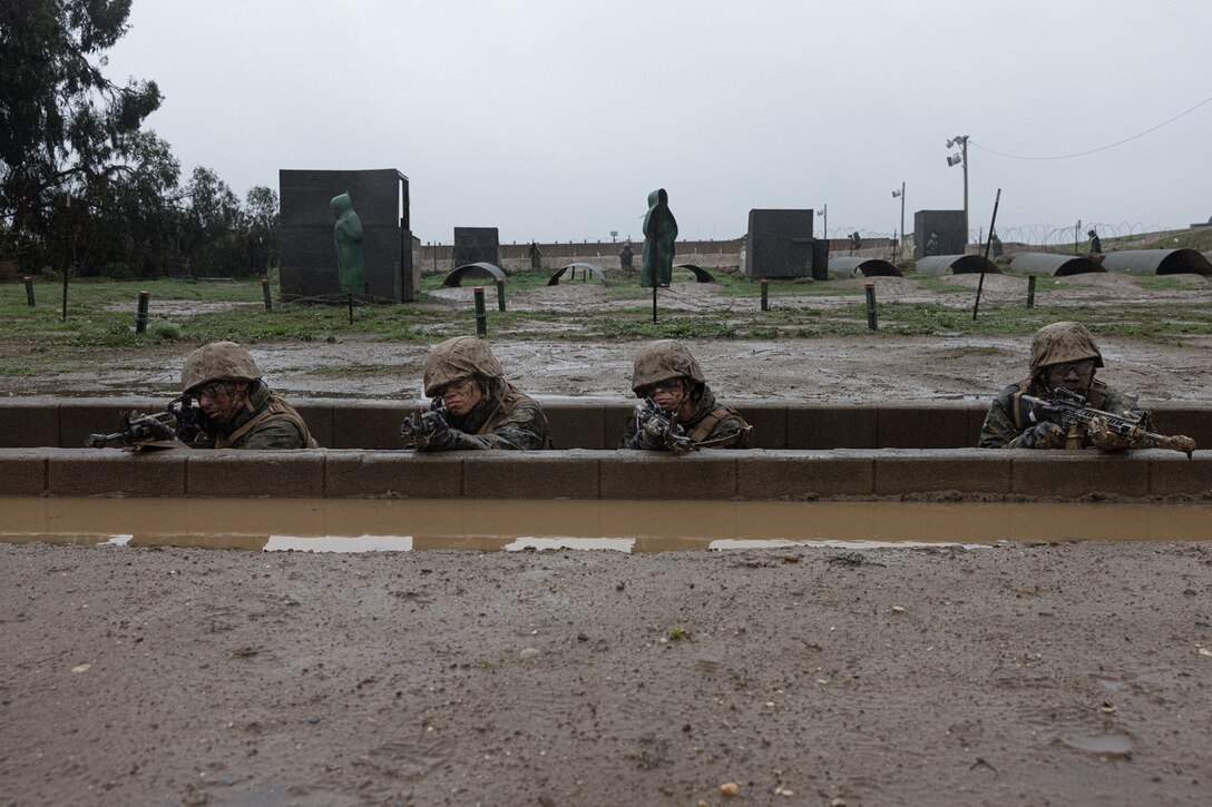 Marine Corps recruits aim their weapons while in a trench.