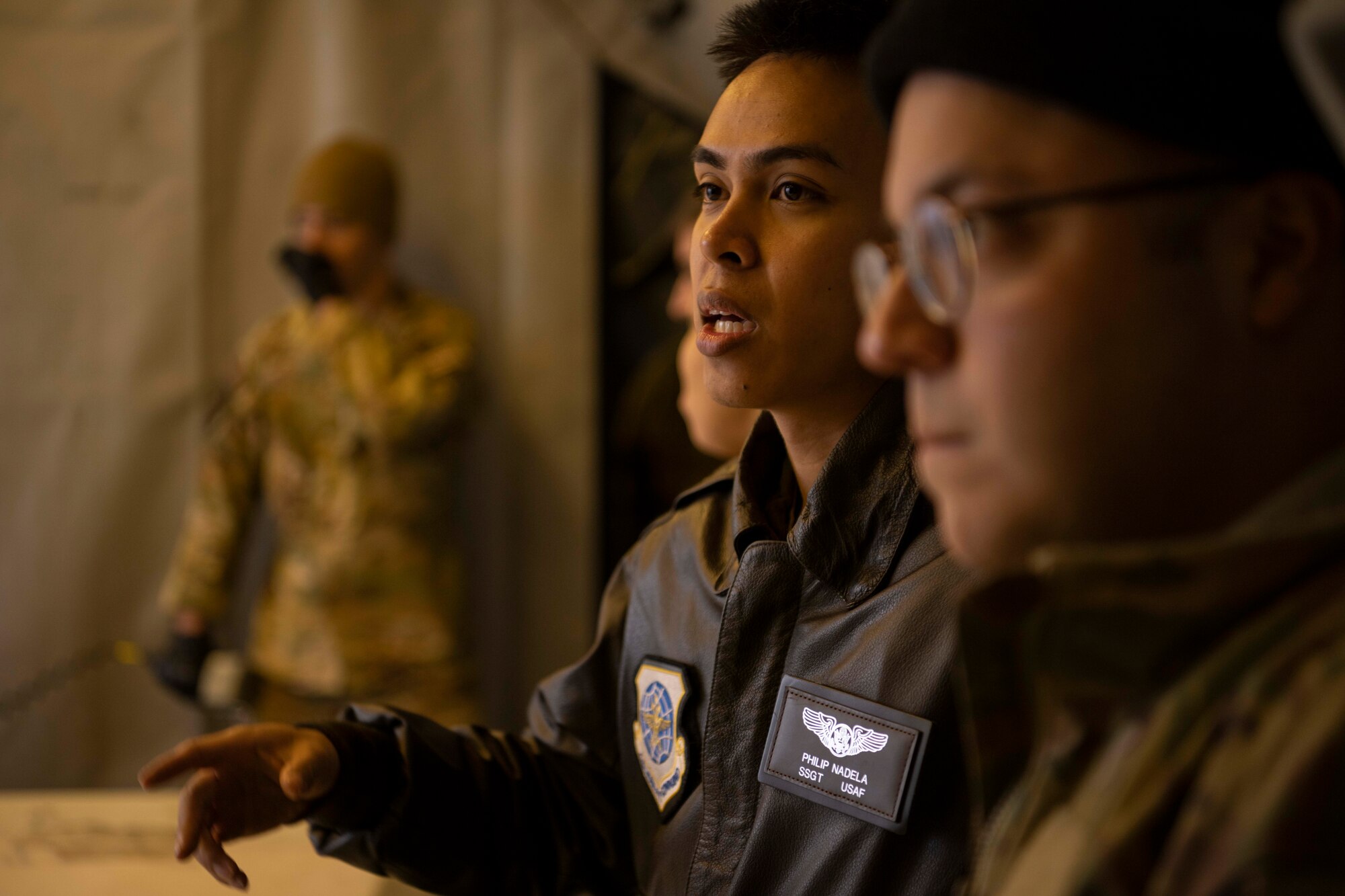 Military members are discussing processes of loading cargo, the members are lined up while one member is featured as they are doing the speaking.