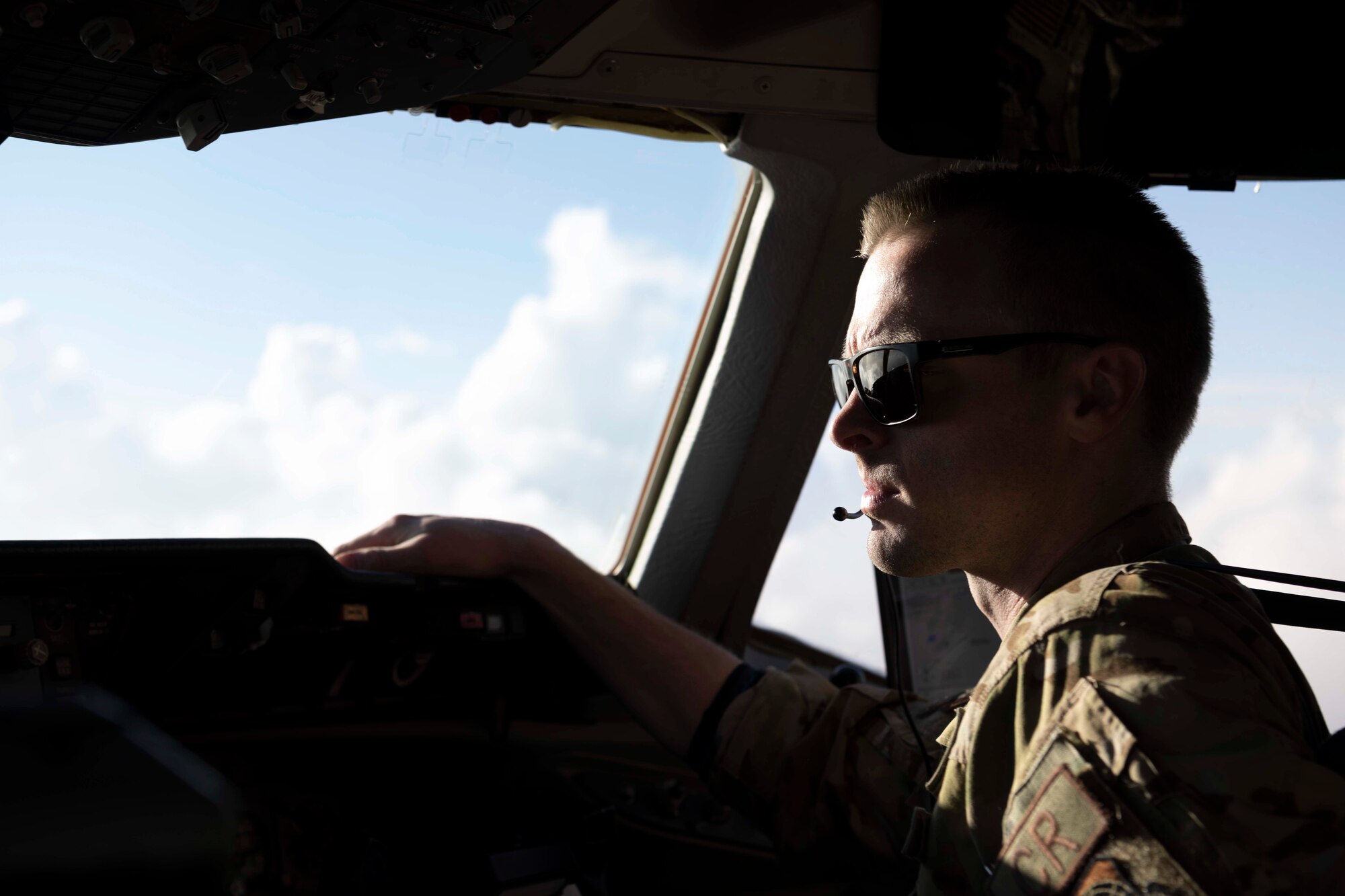 A military member wearing sunglasses sits in a chair on the flight deck while looking out the window.
