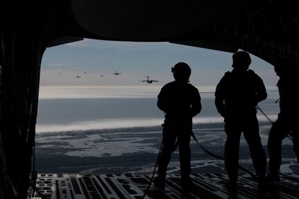 A photo of three Airman watching several C-17s flying from the back of another C-17.