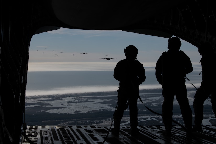 A photo of three Airman watching several C-17s flying from the back of another C-17.