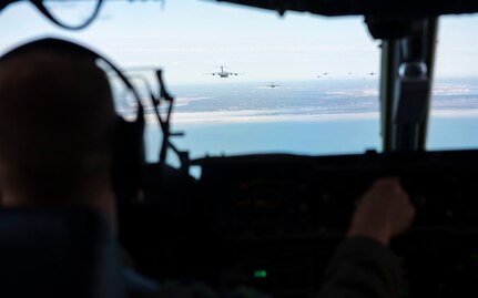 A photo of the view out of the cockpit of a C-17 with several more C-17s flying out ahead.